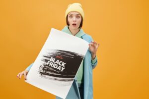 Une jeune femme tient une affiche de vente du Black Friday, surprise sur un fond jaune.
