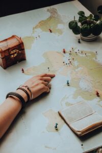Main pointant sur une carte du monde entourée d'éléments essentiels de voyage, suscitant un sentiment d'aventure.