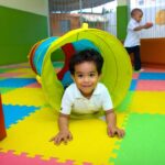 Un enfant rampe dans un tunnel jaune sur un tapis de mousse coloré dans une aire de jeu