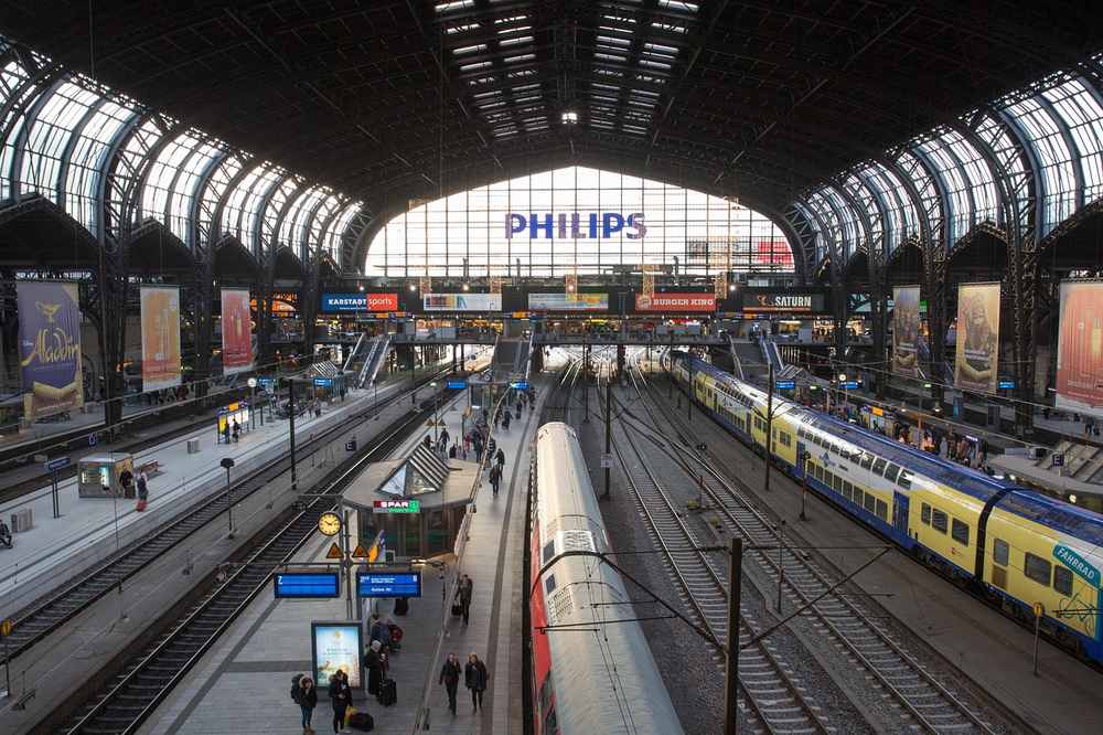 Intérieur d'une gare avec trains, voies et voyageurs sous une grande arche