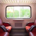 Intérieur de wagon de train avec sièges rouges face à face et grande fenêtre donnant sur la nature