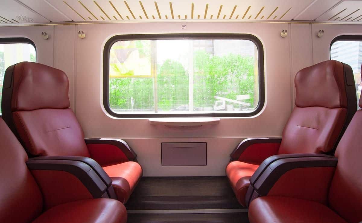 Intérieur de wagon de train avec sièges rouges face à face et grande fenêtre donnant sur la nature