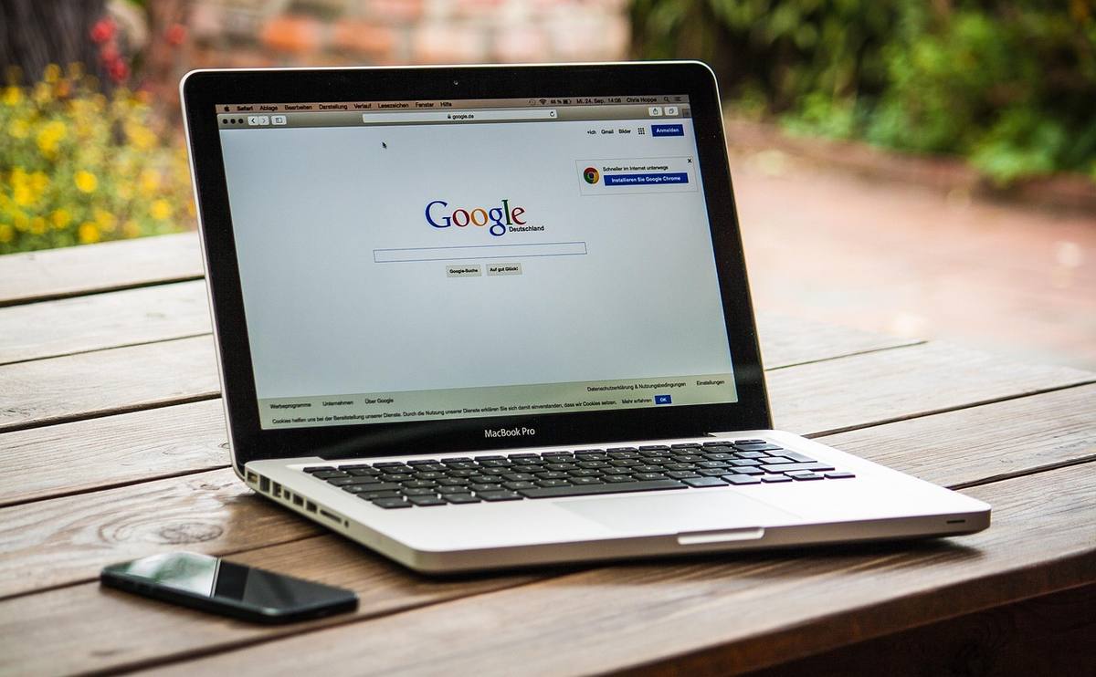 Un ordinateur portable affichant Google, posé sur un banc en bois à l'extérieur