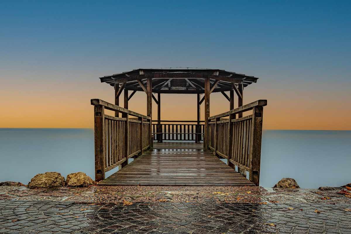 Banc de bois menant à un kiosque au bord d'une mer calme