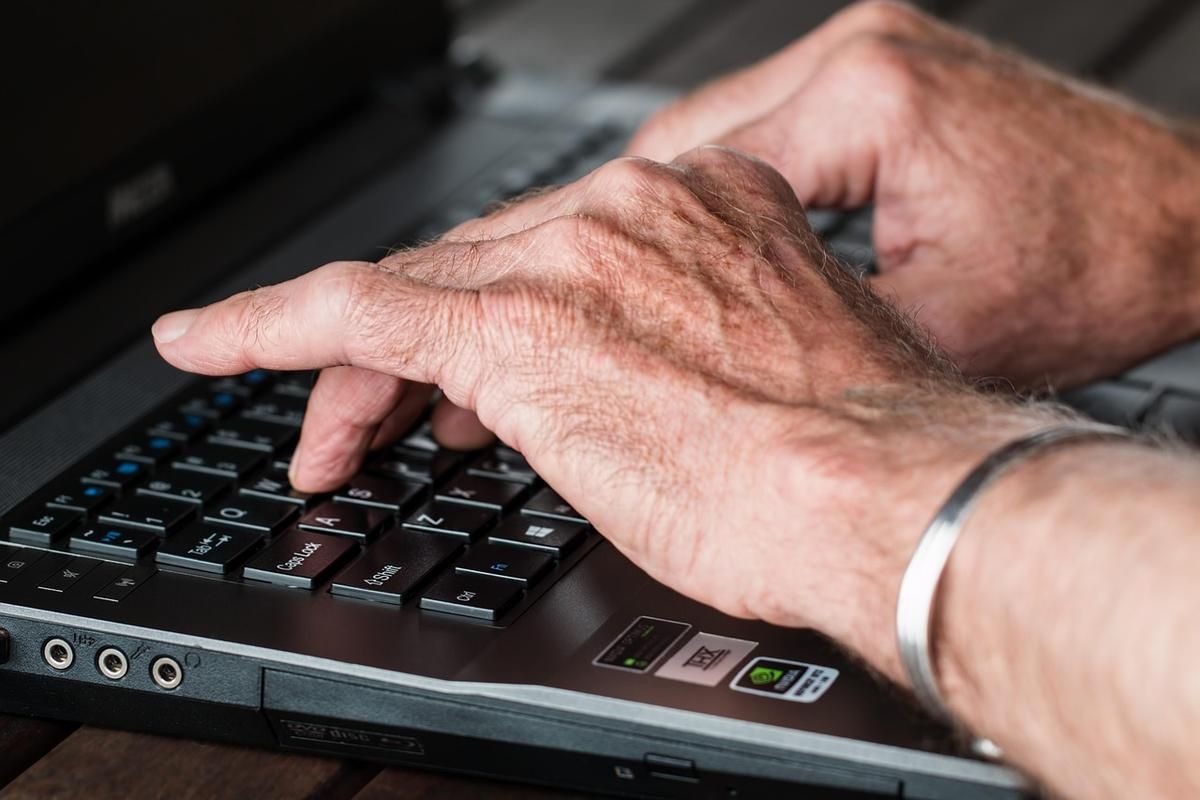 Des mains ridées tapent sur le clavier d'un ordinateur portable